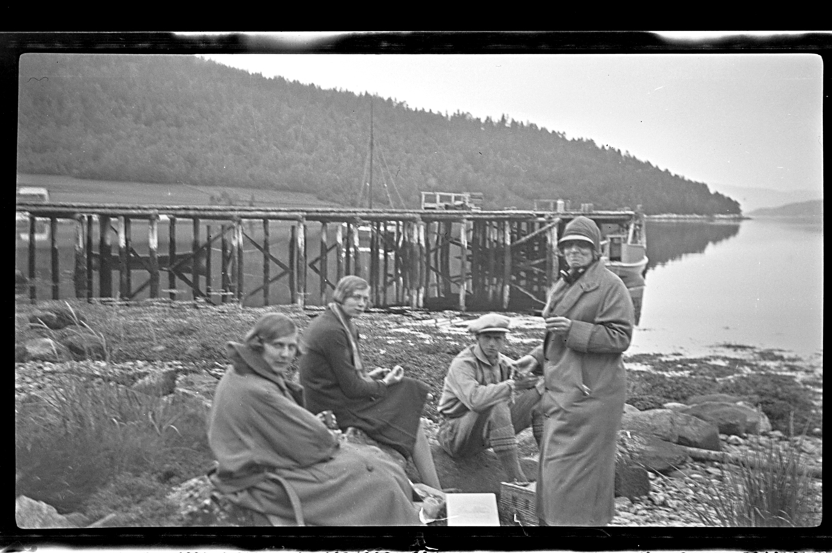 Rolf Sr. Sundt, Hilda Sundt, Julie Thaulow (Lillemor) Aubert, Ferdinand Aars og Birgitte Aubert sitter i strandkanten ved en brygge (kjerrat). Fotografert 1926.