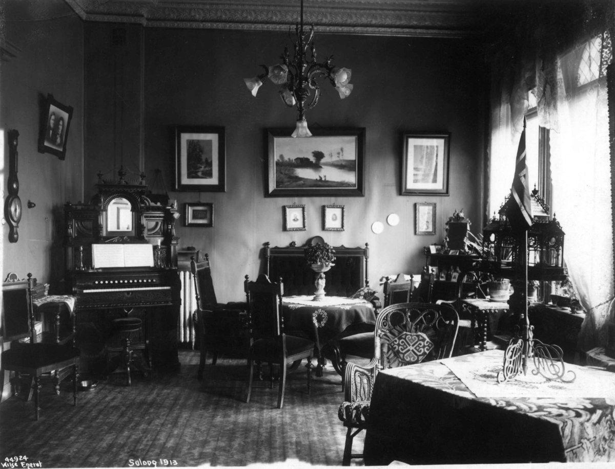 Anders Beer Wilse, Antakelig fra fotograf Anders Beer Wilse sin salong på Drammensveien. Salong interiør 1913. Møbler, piano, bordflagg og bilder.