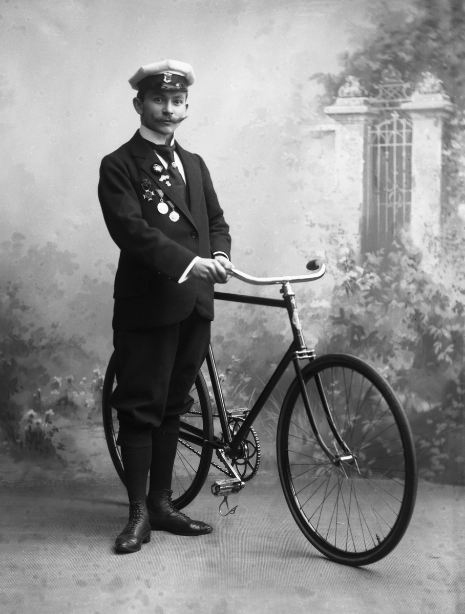 Gustav Borgen, Portrett, mann med uniformslue, medaljer og sykkel.