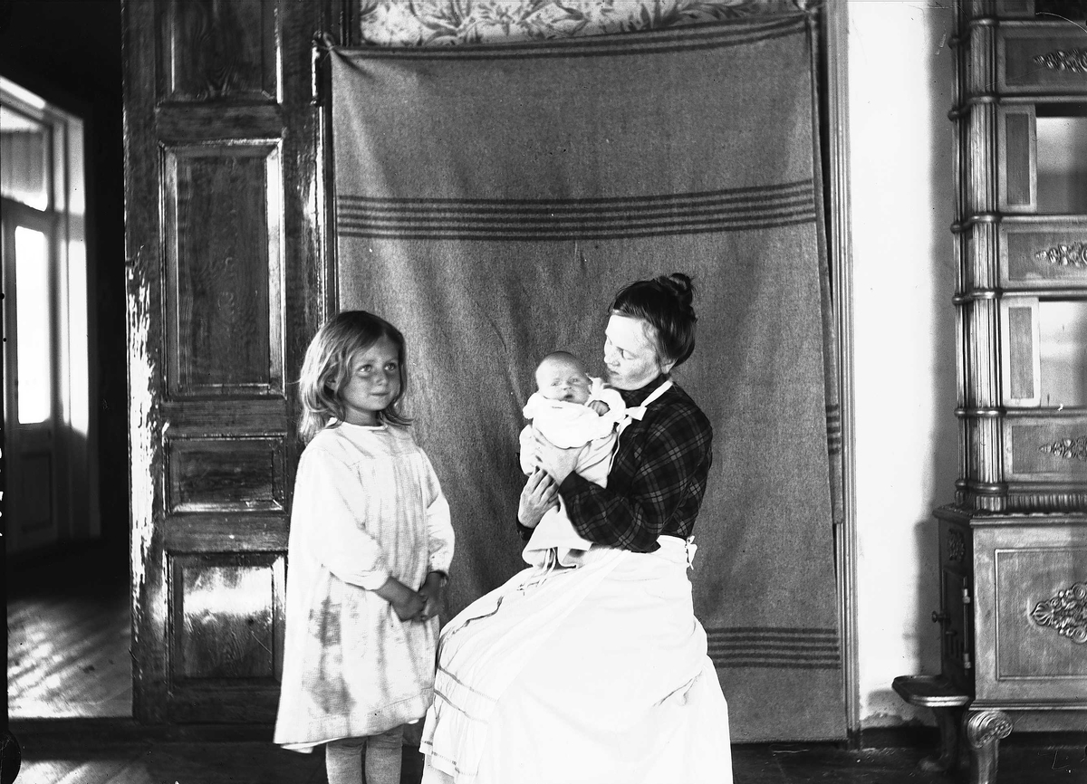 Axel Quinsgaard Wiborg, Interiør, Nedre Digerud, Frogn, Akershus, 1902. Gudrun og Margrethe Q. Wiborg med Halvor Nicolai fotografert mot opphengt teppe.