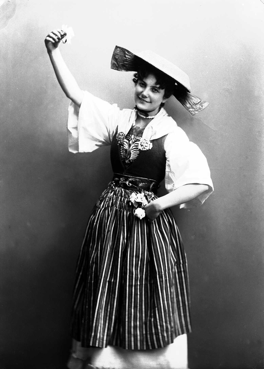Solveig Lund, Kvinne i drakt og hatt, med blomst i hendene.