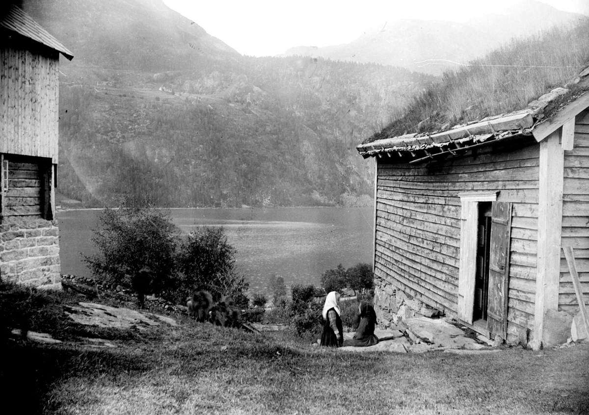 Juliane Fredrikke Langberg, Fra Eggedal, Sigdal, på besøk hos Th. Kittelsen. Gårdstun med med 2 jenter, den ene i hvitt skaut (se flere motiver med henne). I bakgrunnen vann- og fjellparti. Fra malerinne Juliane Fredrikke Langbergs samling, tatt 1895-1910 med motivkrets slekt og venner samt steder tilknyttet samvær med disse.