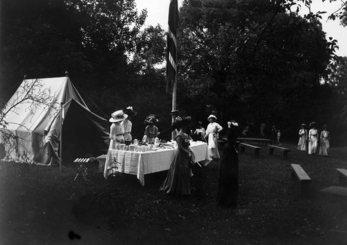 Hermann Christian Neupert, Hovedøya, Oslo. 1908-1910. Sommermotiv. Fest. Festkledde kvinner. Dekket bord. Flagg.