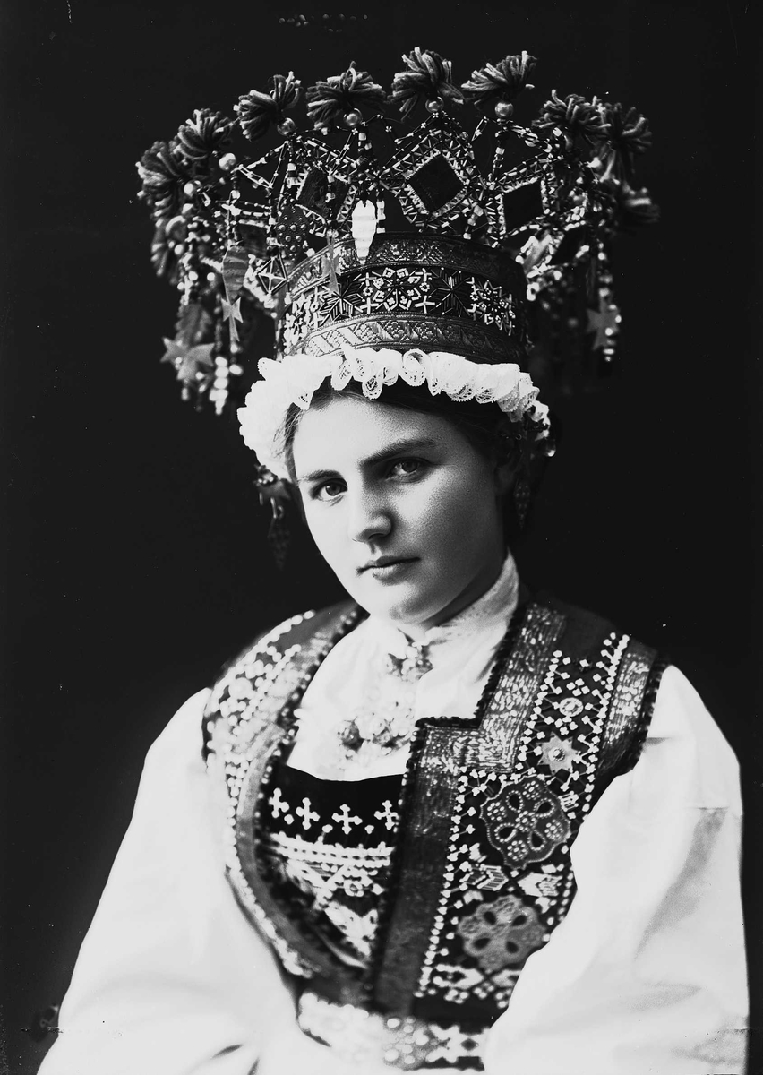 Solveig Lund, Studiofotografi av kvinne med brudedrakt og brudekrone fra Voss i Hordaland. Sittende. Bryst/hofteutsnitt. Vendt mot venstre. Ser ut av bildet.
