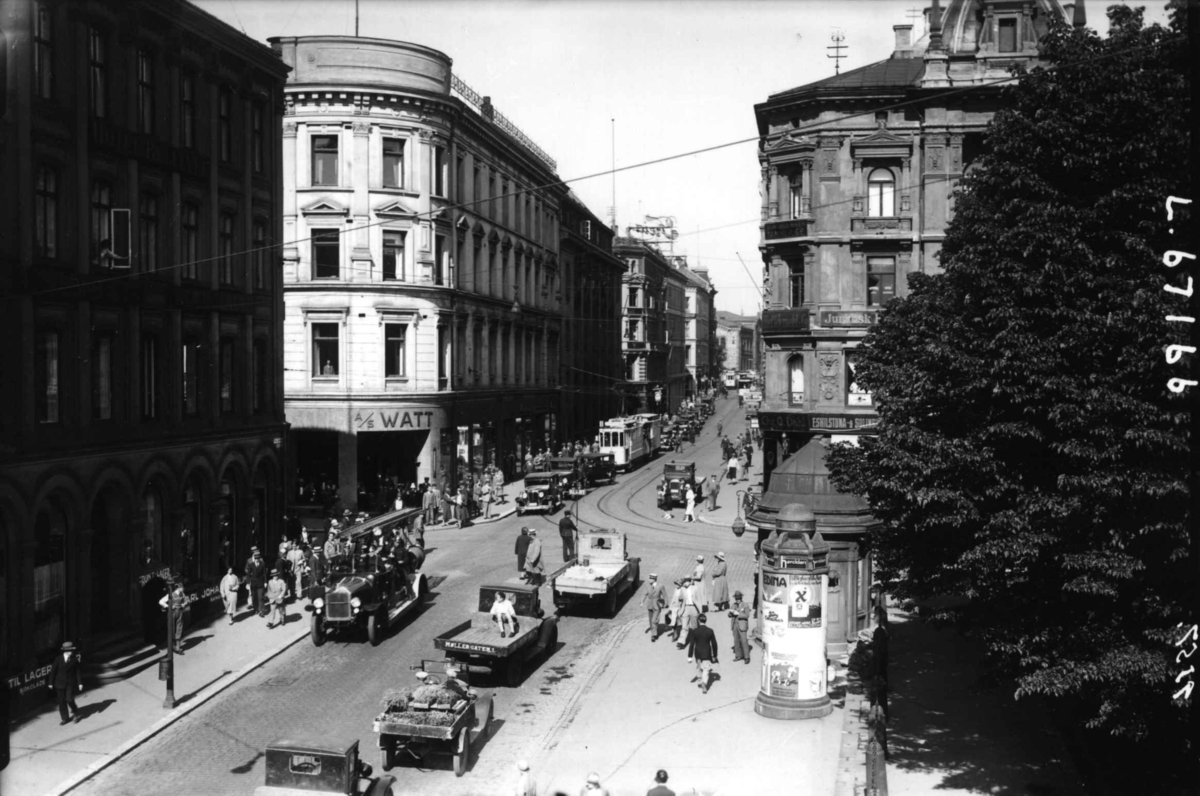 Hermann Christian Neupert, Karl Johans gate, Oslo. Gatebilde fra nedre del med fotgjengere, biler og trikker.