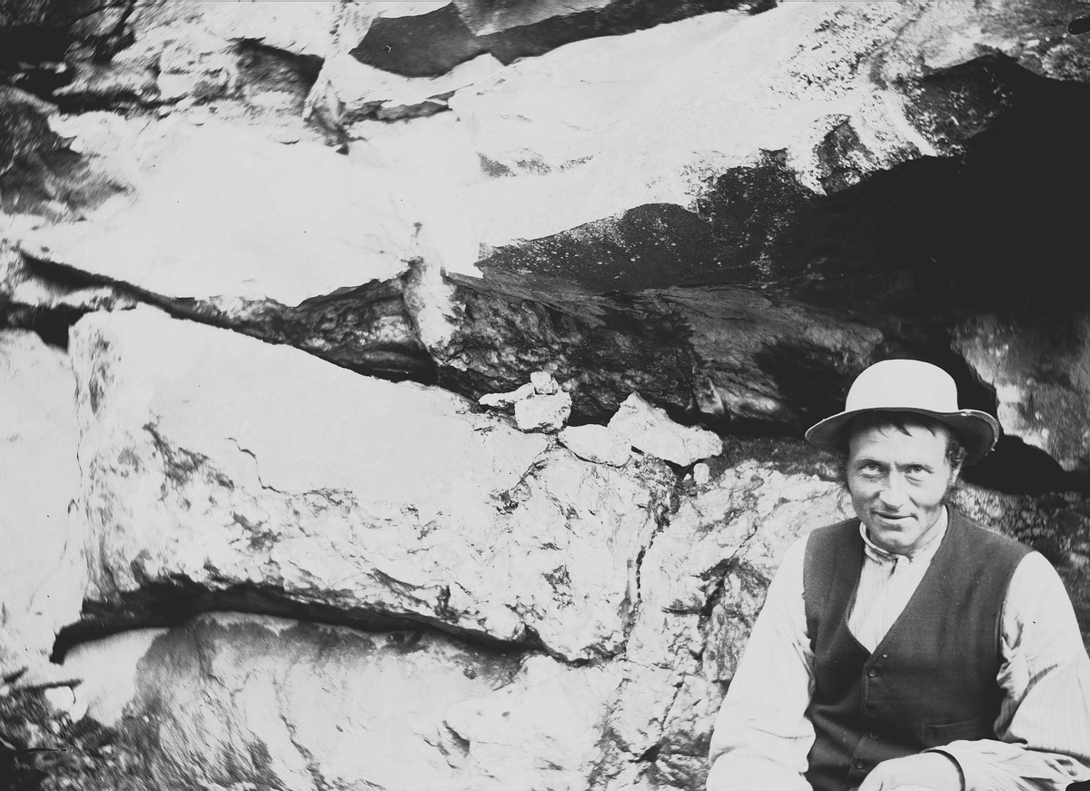 Axel Quinsgaard Wiborg, Nils B. Svensrud, fra Svensrud, Nore, Numedal, Nore og Uvdal, Buskerud, august 1906. Mann sitter foran bergvegg, ved kobbergruve.