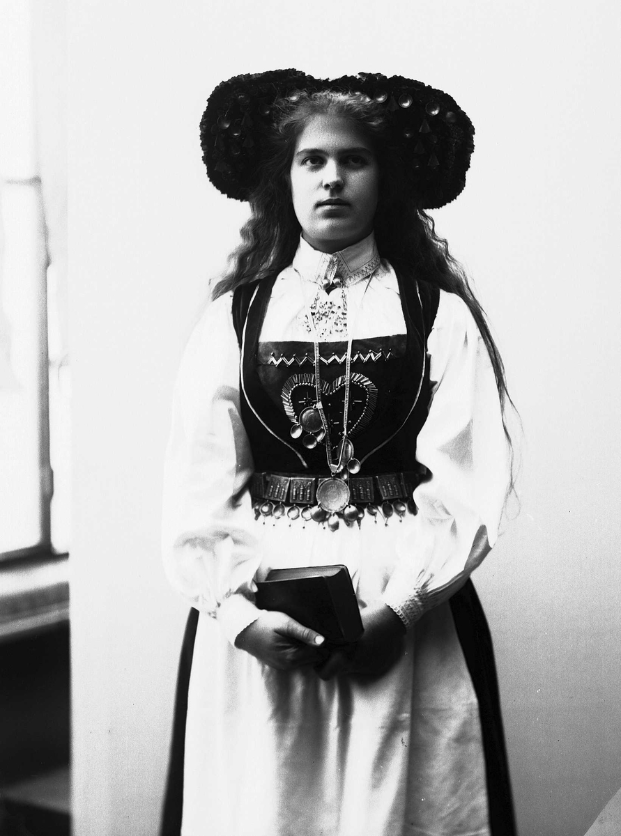Solveig Lund, Studiofotografi av kvinne med brudedrakt og brudehatt på hodet. Holder salmebok/bibel i hånden. Stående 3/4 utsnitt. Frontalt vendt. Ser ut av bildet.
