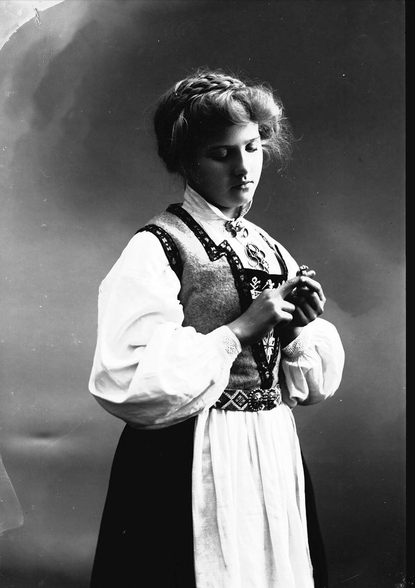 Solveig Lund, 3/4 dels studioportrett av kvinne i drakt, med oppsatt hår. Hun tar på seg en ring. Bakgrunnen er nøytral.
