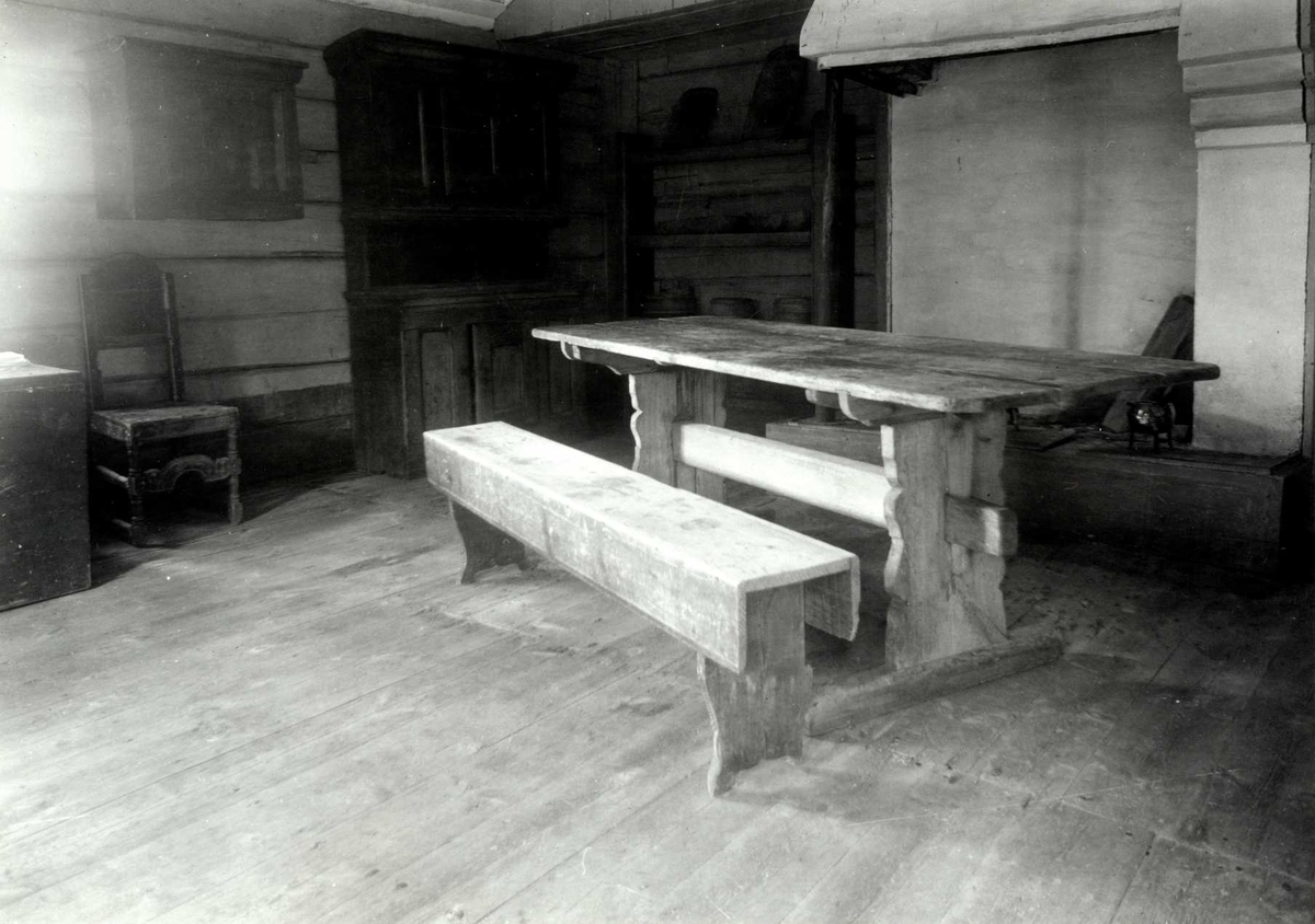 Gisle Midttun, Lømo, Elverum, Sør-Østerdal, Hedmark. Interiør fra stue med bord, benk, peis, skap, hyller og bord. Nå på Glomdalsmuseet.