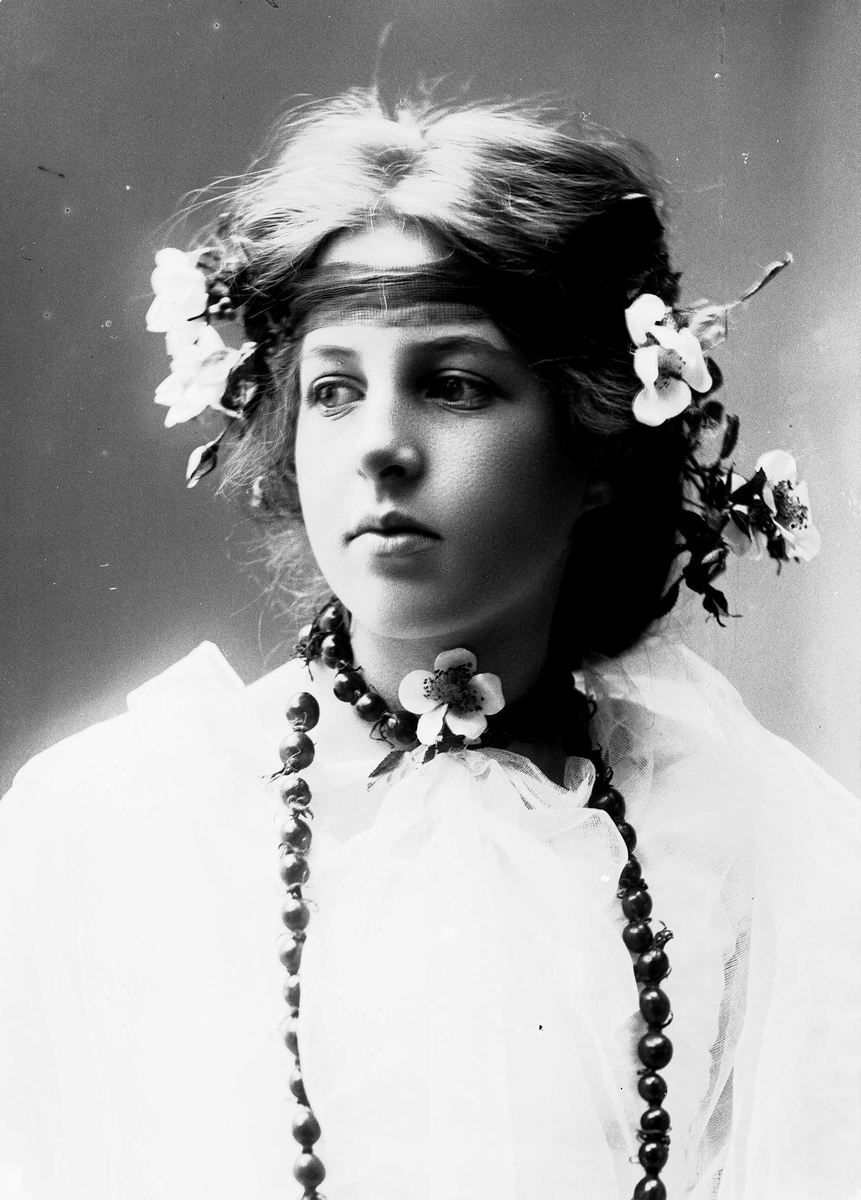Solveig Lund, Studioportrett av kvinne i drakt med blomster i håret og halssmykke.