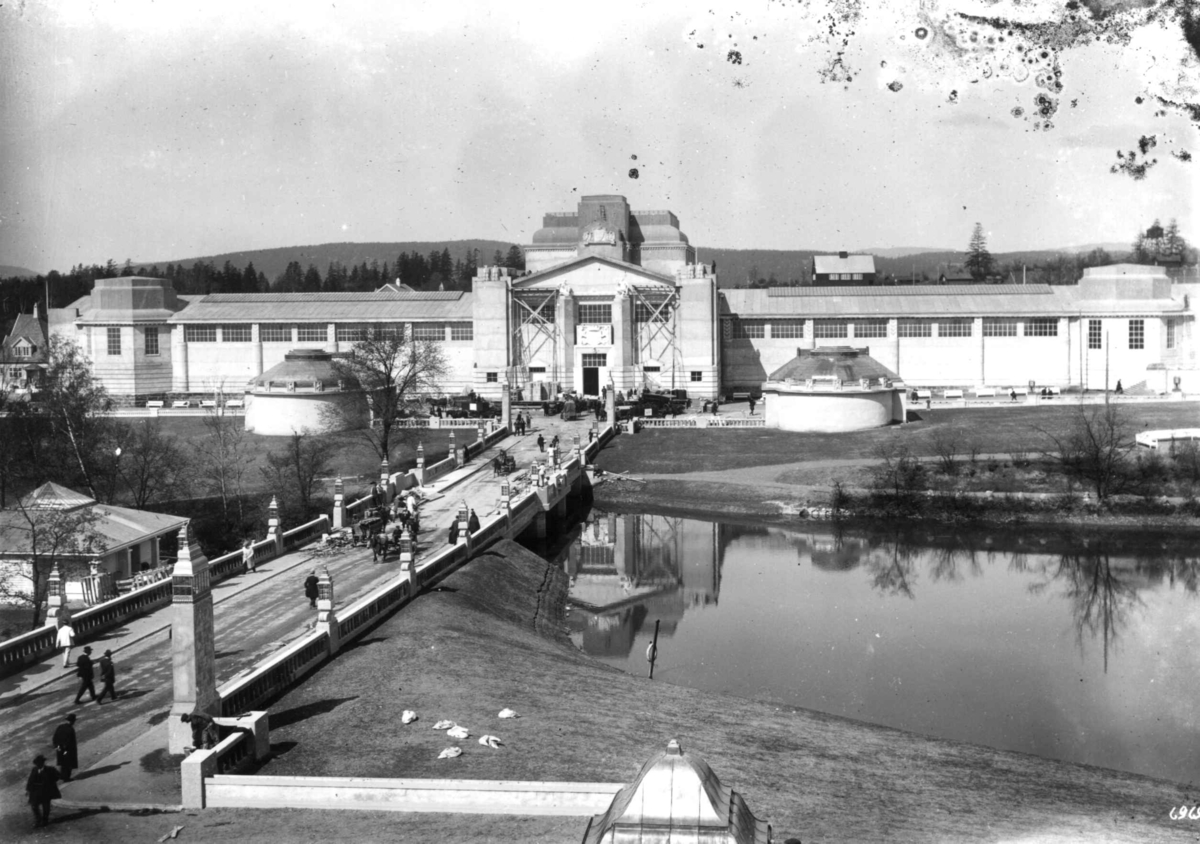 Hermann Christian Neupert, Jubileumsutstillingen på Frogner, Oslo, 1914. Parkområde med bro over til Industribygningen i bakgrunnen. Publikum spaseser på broa. I forgrunnen større dam.