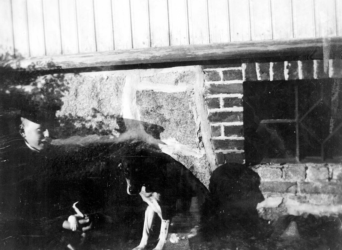 Juliane Fredrikke Langberg, Portrett av gutt med skyggelue og hund foran husmur med vindu med jernsprosser. Christian L. Holm er fotografens nevø, sønn av sognepresten. Ant. på Hurum prestegård. Fra malerinne Juliane Fredrikke Langbergs (1856-1930) samling, tatt ca.1895-1910 med motivkrets slekt og venner samt steder tilknytt…