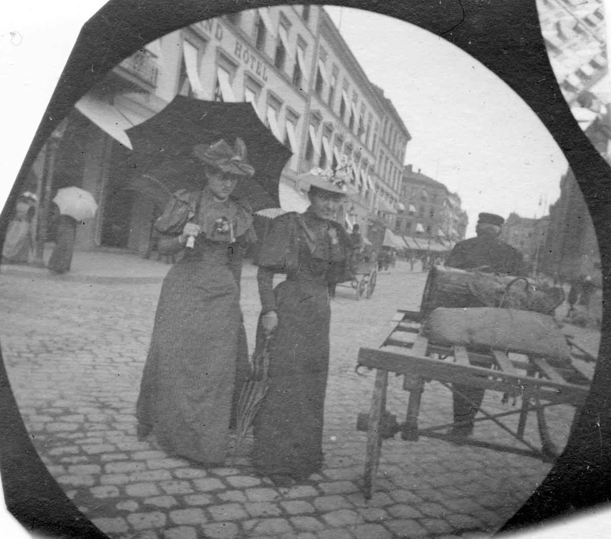 Fredrik Carl Mülertz Størmer, Frk. Lilla Heiberg og frk. Strøm krysser Karl Johan, Oslo. Mann med håndkjerre og hestevogn.