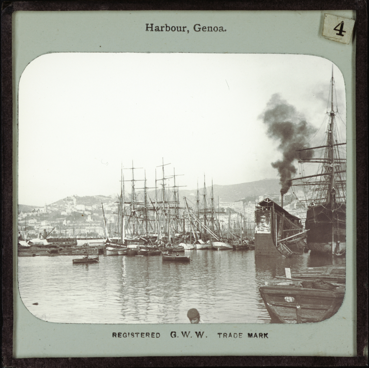 G.W.W., Bild från Italien föreställande hamnen Genua, "Harbour, Genoa". I hamnen finns enbart segelfartyg, men tjock svart rök, kanske från ett ångfartyg, stiger upp bakom en av de utskjutande pirerna. I bilden mitt syns två roddbåtar. Registered G.W.W. Trade Mark.