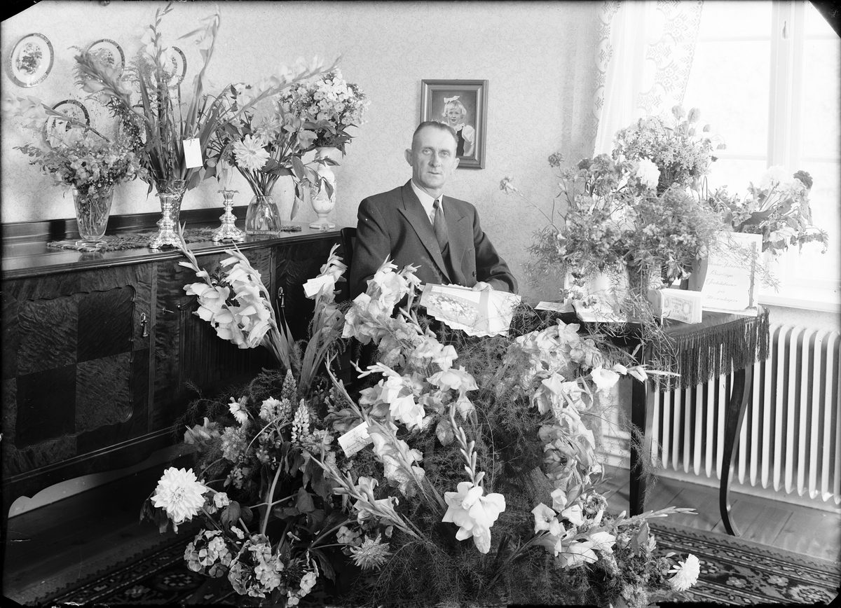 Skötsner-Edhlund, Elmontör Valdemar Johansson omgiven av blommor, Gimo, Uppland