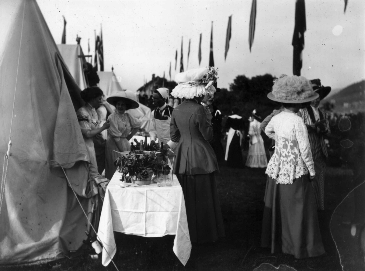 Hermann Christian Neupert, Hovedøya, Oslo. 1910. Sommermotiv. Fest. Festkledde kvinner. Telt. Flagg.