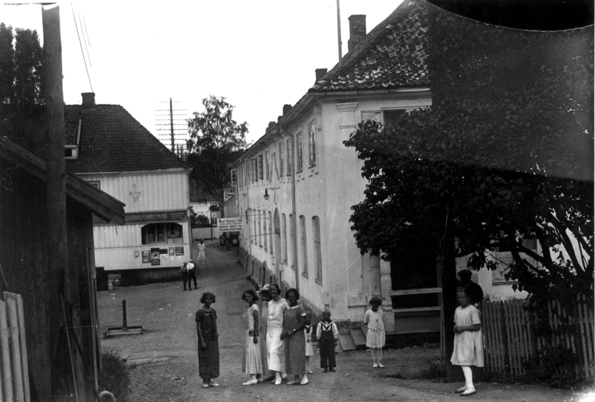 Hermann Christian Neupert, Son, Vestby, Akershus 1924. Bildet viser torget i Son. Festkledde mennesker foran hvite bygninger. Spinnerigården til høyre brant 17.mai 1976. Bygningen ble gjenreist. Til høyre ligger Thornegården.