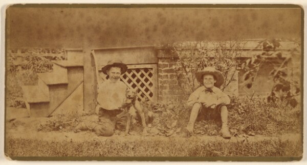 Unknown, [Two boys seated on ground with a dog]