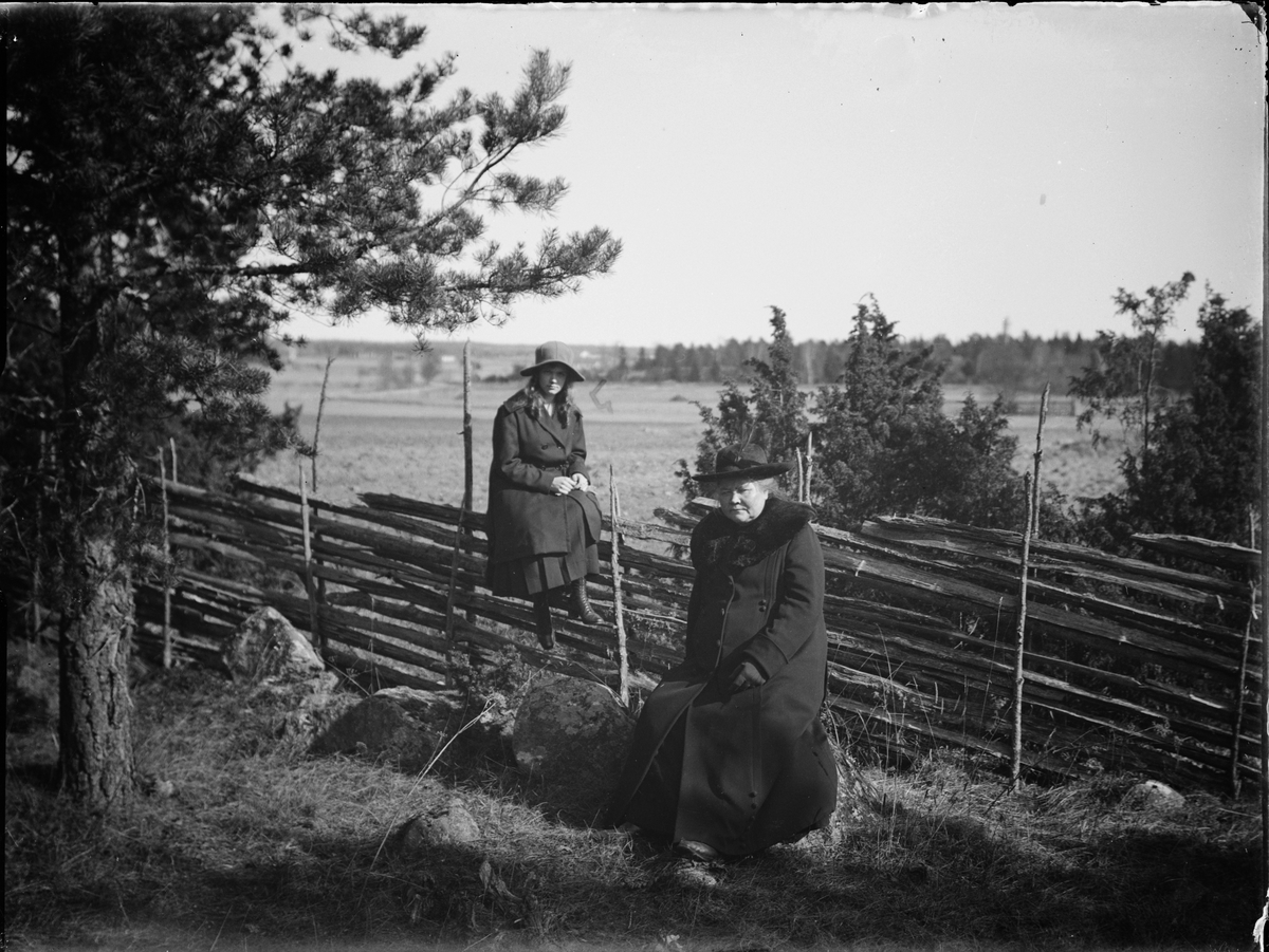 Skötsner-Edhlund, En kvinna sitter på gärdesgården och en kvinna sitter på en sten, Östhammar, Uppland