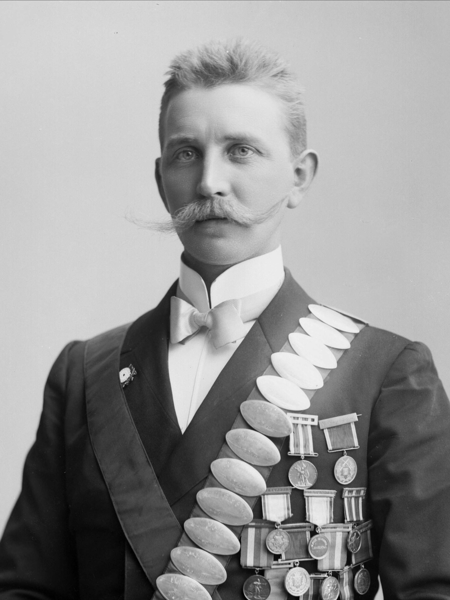 Gustav Borgen, Portrett, mann med bånd med premieplaketter, skyting. Kongebeltene til Skydeselskapet Skarpskytten. Carl Chr Engelstad.
