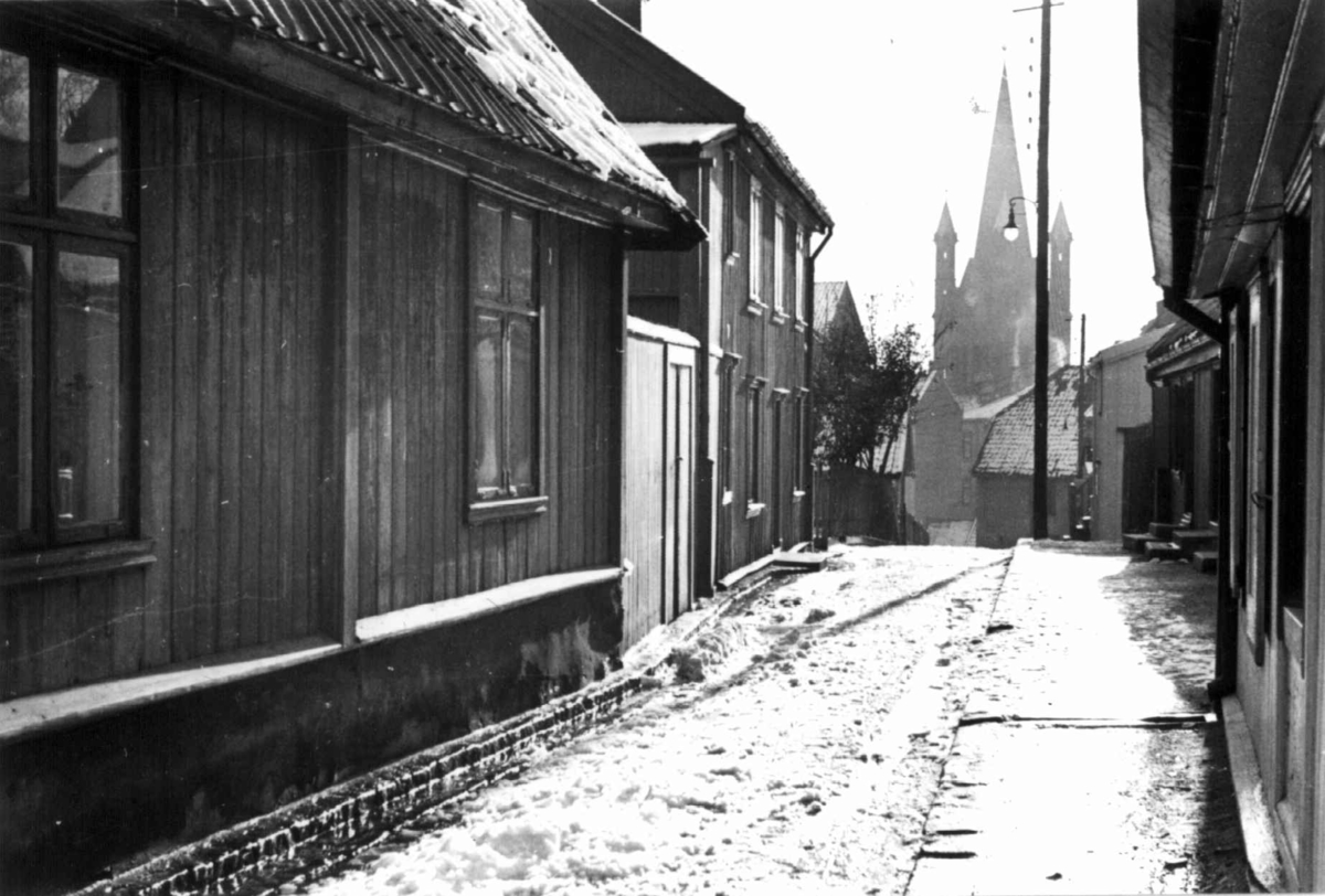 Anders Beer Wilse, Langeleiken, Enerhaugen, Oslo 1935. Smal snødekket gate mellom husene mot Grønlands kirke.