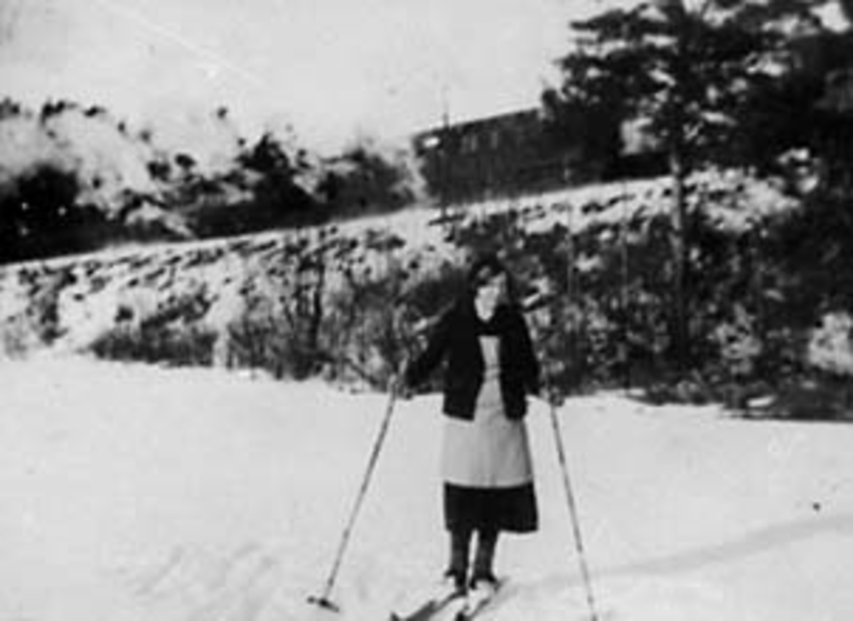 Anno Domkirkeodden, PORTRETT: JORUN KNUTZEN FØDT: HÅKENSEN PÅ SKI I KJOLE MED FORKLE, FURUHOLTE, VINTER