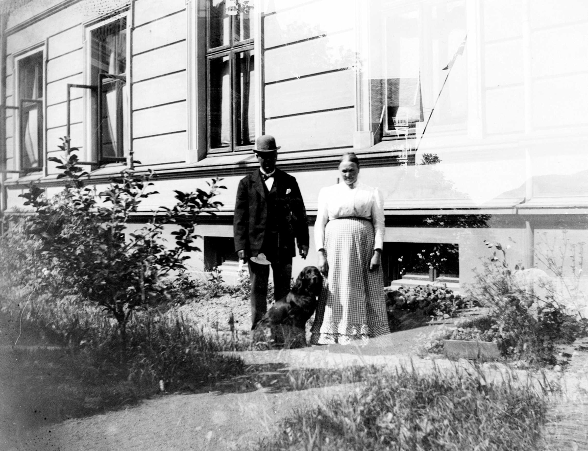 Juliane Fredrikke Langberg, Eldre par med hund poserer foran bygård med hageparti. Personer og sted ukjent. Fra malerinne Juliane Fredrikke Langbergs (1856-1930) samling, tatt ca.1895-1910 med motivkrets slekt og venner samt steder tilknyttet samvær med disse.