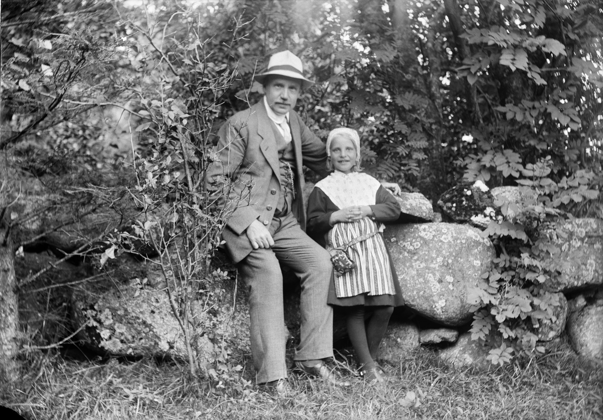 Okänd,, Ruben Liljefors seated on a stone wall with his daughter Marit, dressed in folk costume, next door, probably in Dalarna