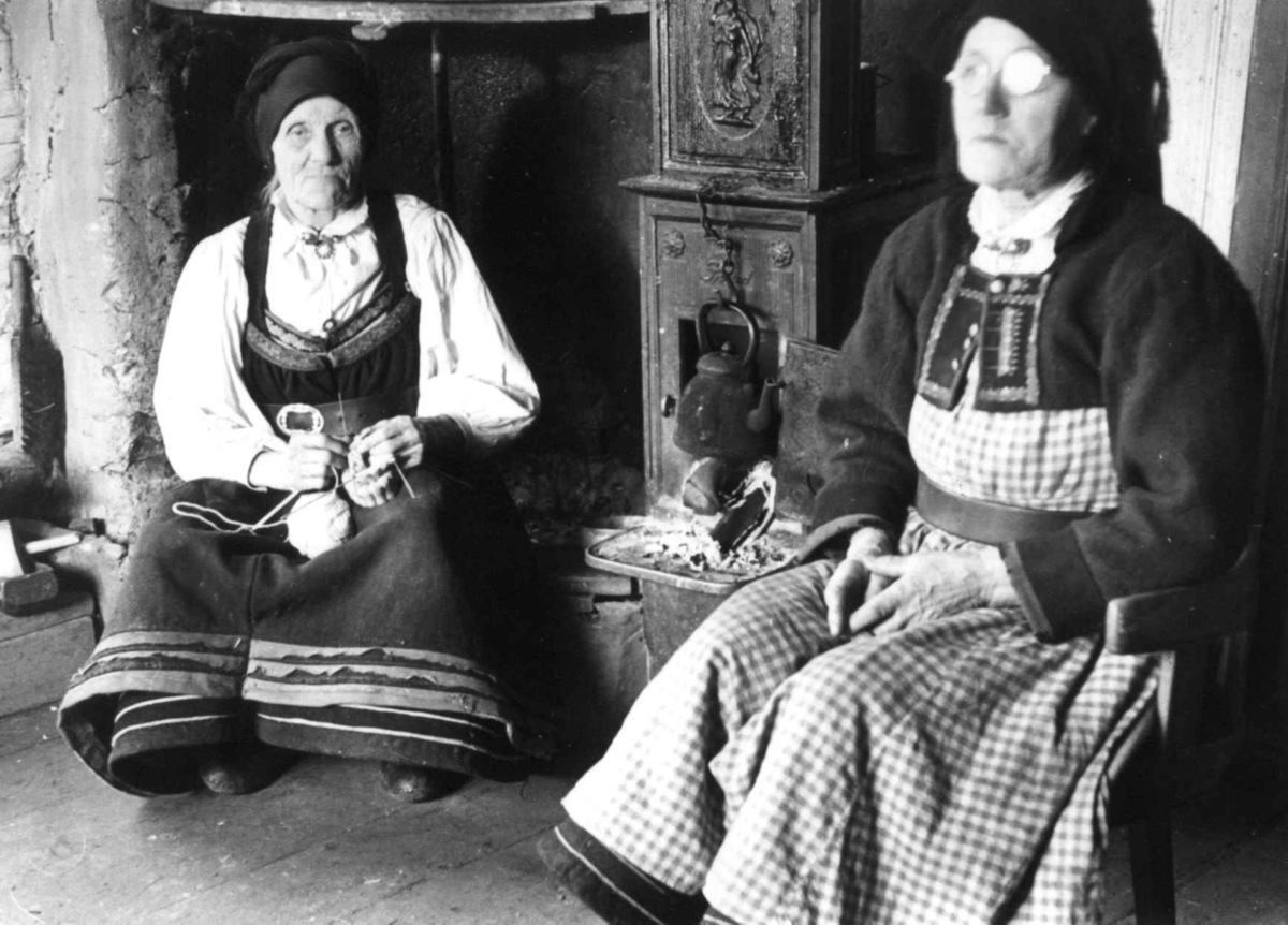 Anna Grostøl, Valle, Aust-Agder 1938. Kaffekoking. To kvinner sitter ved grua. Vanlege klæde ein kjøleg haustdag. Kaffi- kokar. har nett vore brukt. Frk. Ingeborg Skeivollen, Valle.