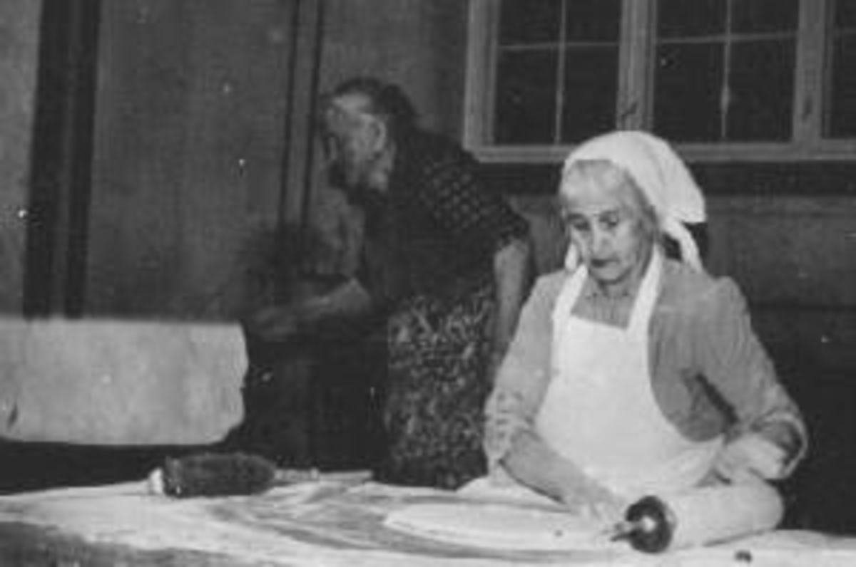 Anno Domkirkeodden, Interiør. kjelleren i internatet på Grefsheim, Nes, Hedmark. Bergine Pedersen f.1891 baker lefse mens Hilda Solberg steker. De bakte mange steder og var veldig nøye med baksteveden. Johan Engen måtte kløyve den på Grefsheim. Bakstebord, kjevle, kost, takke, bakstekoner, forkle, skaut.