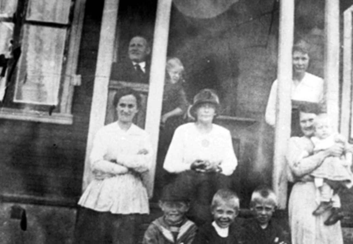 Anno Domkirkeodden, Gruppe, familie, veranda, Briskebyvegen 25 i Hamar. Foran 1 rekke fra v. Kåre Knudsen. På armen til h. Einar Knudsen holder barnet Anne Knudsen. Bak på veranda til h. Elise Strand, sittende i midten Oline Svenkerud.