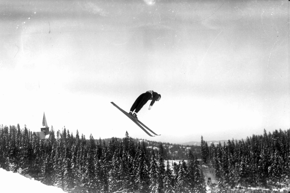 Hermann Christian Neupert, Holmenkollrenn. 1934. Hopper i svevet. Nordmarka og Holmenkollen kapell ses i bakgrunnen.