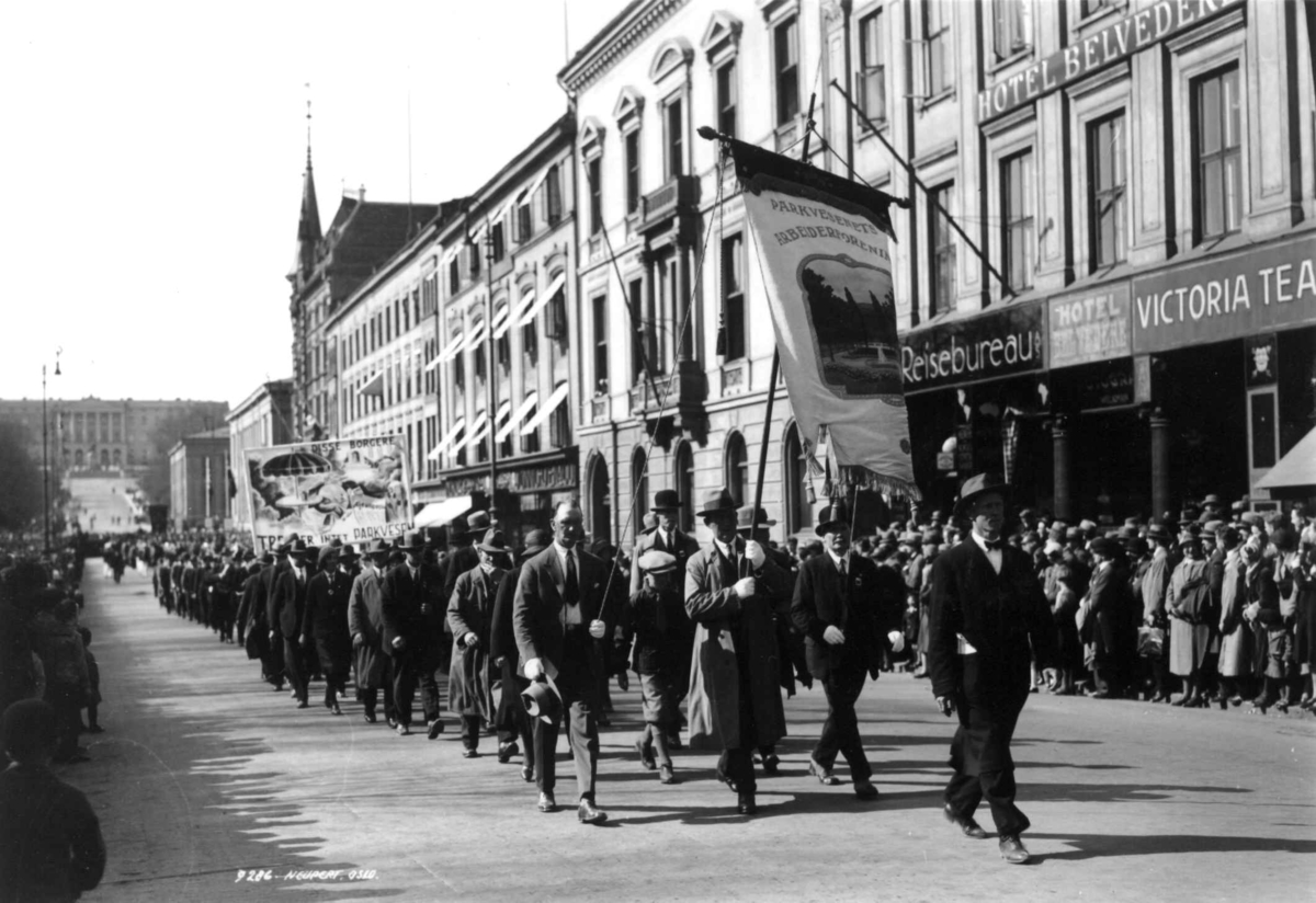 Hermann Christian Neupert, 1. mai-tog. Karl Johans gate. 1930. Slottet i bakgrunnen. Toget på vei mot Stortinget. Menn med faner. Tilskuere.