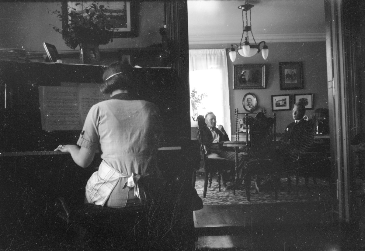 Håkon Prestkværn, Interiør, stue, kvinne spiller piano. Ukjent sted.