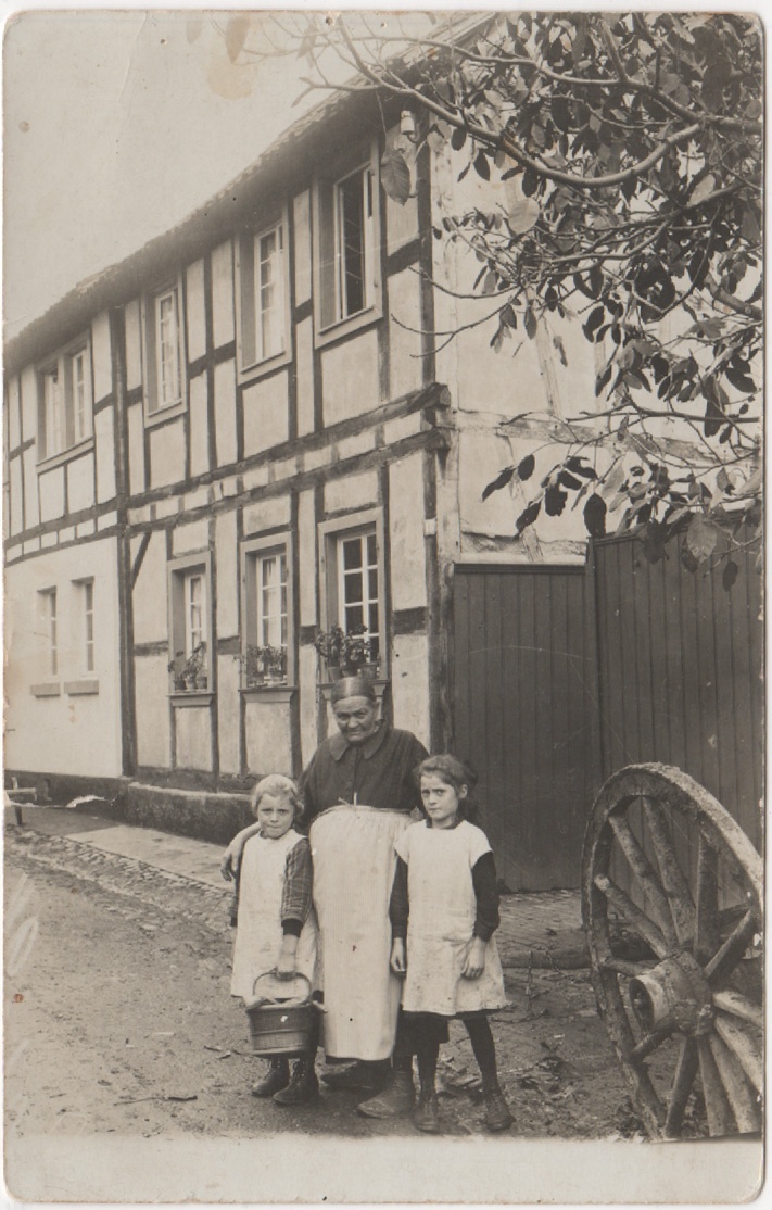 Unknown artist, Ältere Frau mit zwei Enkel vor einer Toreinfahr stehend