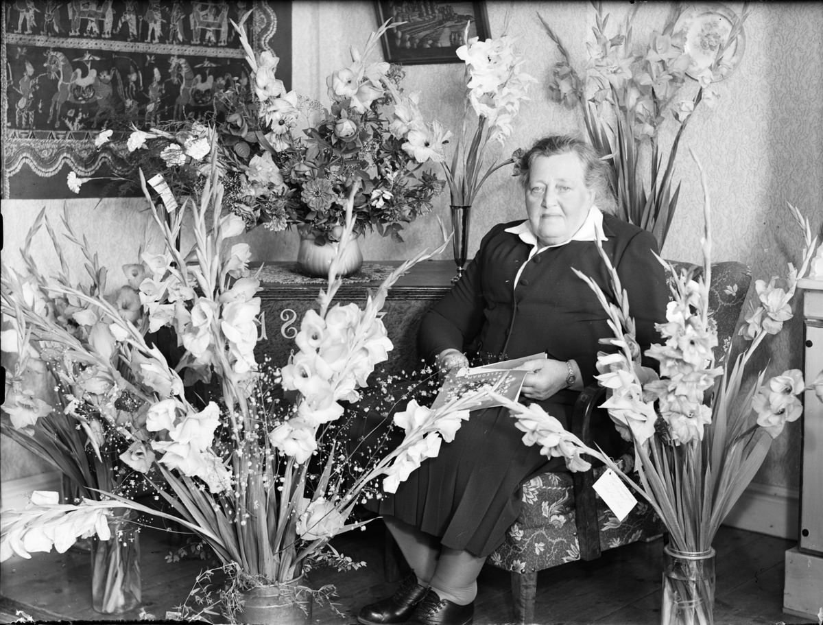 Skötsner-Edhlund, Kvinna i hemmiljö omgiven av blommor firar 70-årsdag, Östhammar, Uppland,