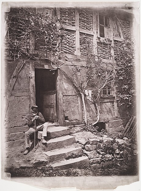 Unknown, [Man Sitting on Steps of House with Socks Hanging on Nearby Vine to Dry]