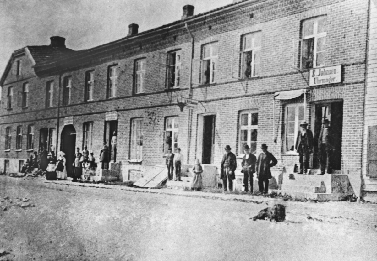 Anno Domkirkeodden, EKSTERIØR LILLE STRANDGATA 3 I HAMAR, FOLK, JOHNSGÅRDEN, URMAKER SIMEN JOHNSENS, GÅRD. MALERMESTER ANDREAS JACOBSEN EIDE GÅRDEN FRA 1849-1861. SKYSS-STASJON, LOSJI, HAMARS FØRSTE HOTEL. KOMMUNALE MØTER, ARREST I KJELLEREN, GÅRDEN BRANDT I 1880. JOHNSEN MED GRÅ HATT PÅ TRAPPA.