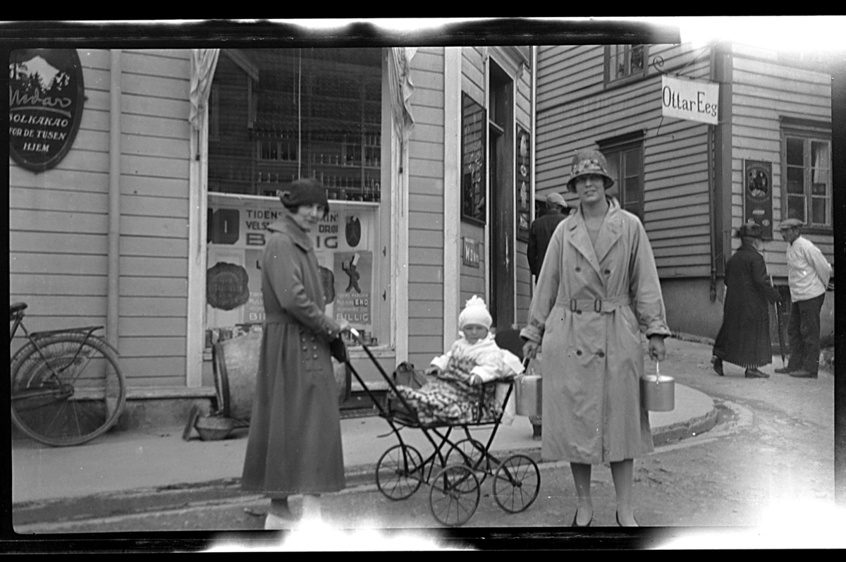 Rolf Sr. Sundt, Arne Moestue sitter i en barnevogn mellom sin tante Hilda Sundt og sin mor Lilly Moestue foran en butikk. Fotografert 1926.