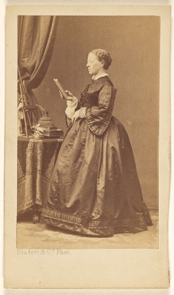 Disdéri & Cie., [Unidentified woman, standing, looking at a book]