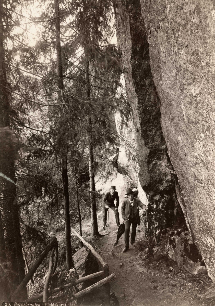 Axel Lindahl, Sarabråten, Østmarka, Oslo. To menn spaserer på vei i skogen, under klippe.