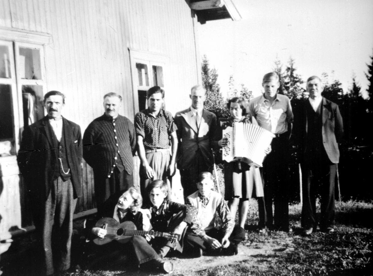 Anno Domkirkeodden, Arbeidsfolk slapper av med musikk, gitar og trekkspill på husmannsplassen Fløttum under Mellom-Kise, Nes, Hedmark. Fra venstre er Petter Lundstein, Johannes Fløttum, Johan Fløttum, Tore Solvang, Guri Bjørklund, Jørgen Fløttum, Kristian Rosenlund. Foran er ukjent, Magne Fløttum, Kåre Rosenlund.