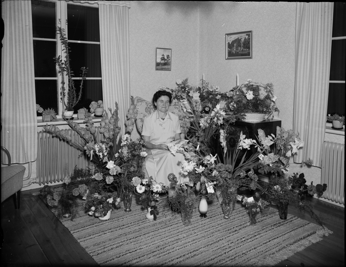 Skötsner-Edhlund, Kvinna i hemmiljö omgiven av blommor, Östhammar, Uppland