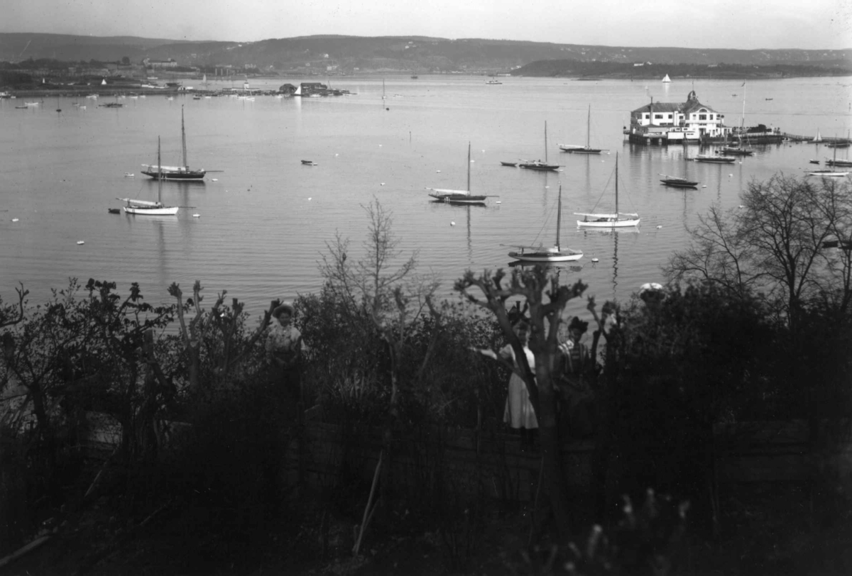 Hermann Christian Neupert, Bygdøy, Oslo 1908-10. Oversiktsbilde. Utsikt mot Dronningen og fjorden. Båter. Kvinner i forgrunnen.
