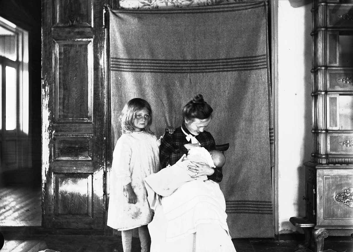 Axel Quinsgaard Wiborg, Interiør, Nedre Digerud, Frogn, Akershus, 1902. Gudrun og Margrethe med Halvor Nicolai Q. Wiborg, fotografert foran opphengt bakteppe.