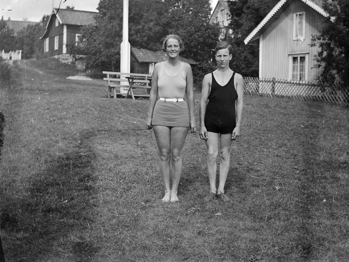 Okänd,, Ung man och kvinna i badkläder står utomhus, gårdsmiljöer, möjligen i skärgård, i bakgrunden, sannolikt i Sverige