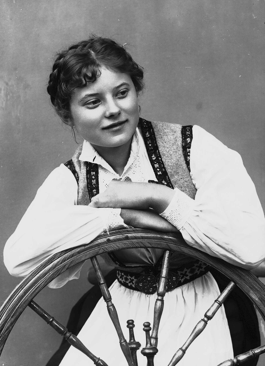 Solveig Lund, Studioportrett av kvinne i drakt, som sitter ved en rokk. Bakgrunnen er nøytral.