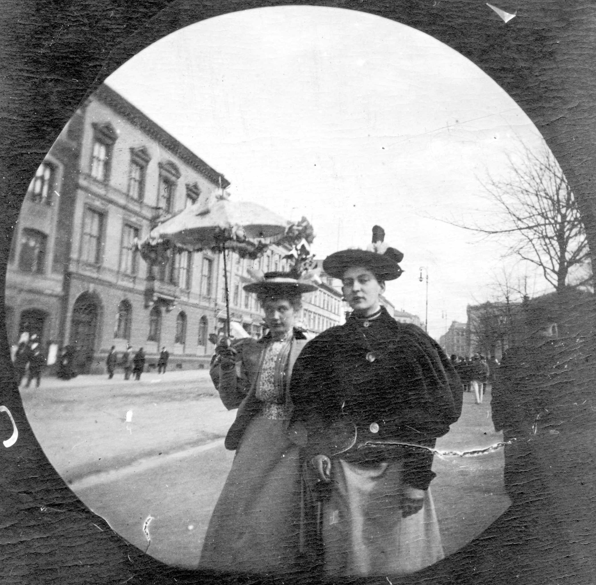 Fredrik Carl Mülertz Størmer, Frk. Irgens og frk. Finne spaserer langs Karl Johans gate, Oslo. Stortinget skimtes bak trærne.