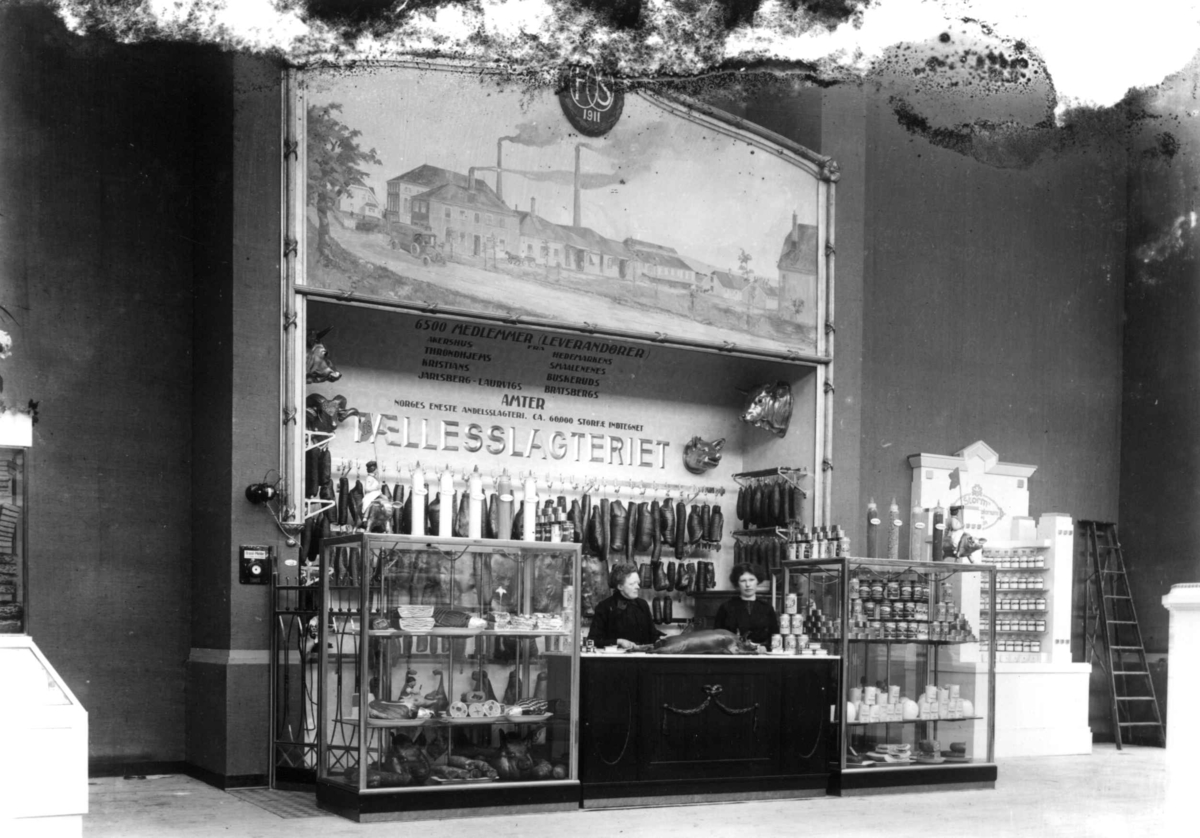 Hermann Christian Neupert, Jubileumsutstillingen på Frogner, Oslo, 1914. Interiør paviljong. Utsnitt av Fællesslageriets utstilling av egne produkter. to kvinner bak disken.
