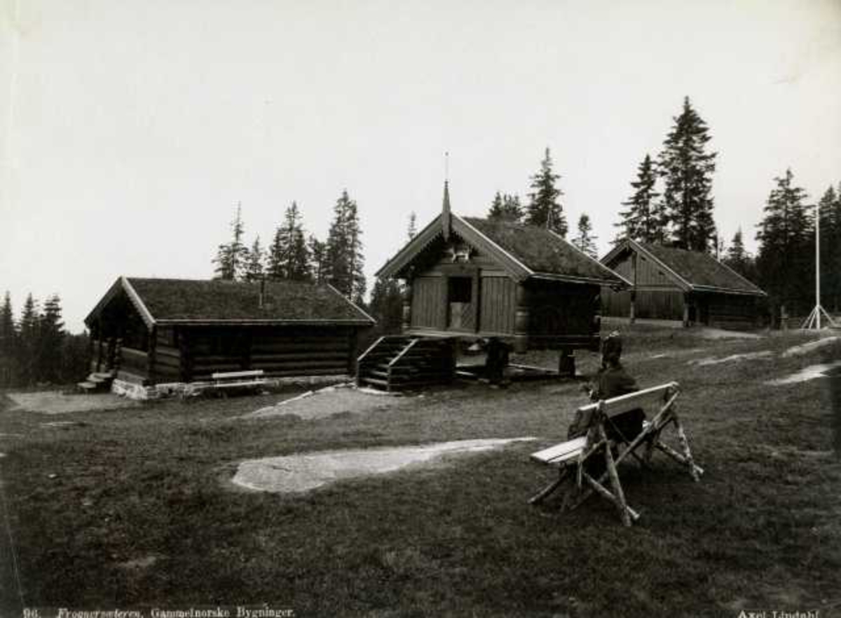 Axel Lindahl, Frognerseteren, Oslo. Avfotografert postkort. Små gamle norske bygninger. Kvinne sitter på krakk.